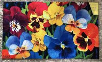 Multicolor floral patterned doormat showing detailed pansy flowers in red, yellow, blue, purple, and orange on a dark background.