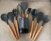 Photo showing eight gray silicone kitchen utensils with wood handles arranged next to a gray silicone utensil holder.