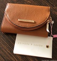 Front view of a compact brown textured wallet with gold-tone brand plate and attached white tag.