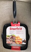 Front view of Starfrit grill pan with packaging showing product name and photo of cooked food.