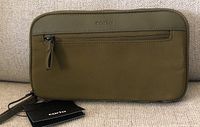 Front closed view of the olive green Carta travel wallet showing external zippered pocket and attached wrist strap with tags.