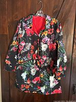 Front view of women's reversible coat hanging on a hanger, showing floral print side with attached tags on right pocket.