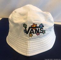White youth size S/M bucket hat with embroidered Vans logo and colorful flowers on front.