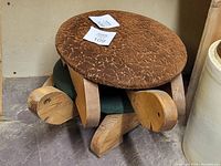 Pair of turtle-shaped wooden footstools with brown cushioned tops placed on a concrete floor.