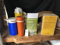 Three vintage thermoses alongside two boxed coffee makers on wooden surface.