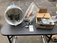 Photo showing white bucket with metal heavy duty wall anchors and a box of Ramset concrete anchors on a black leather surface.