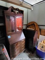 Full view of antique secretary desk with hutch in a storage setting, showing the glass doors and fold-down desk surface.