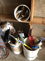 Three buckets arranged on floor and shelf, filled with various brushes and scrapers of different types and sizes.