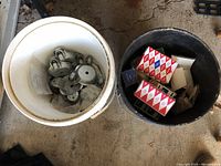 White bucket filled with metal casters and black bucket filled with stapler boxes and staples.