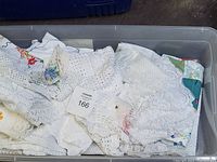 Photo showing a plastic tote filled with white and cream crocheted and embroidered linens, some with lace edges and floral embroidery.