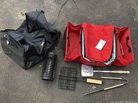 Black nylon duffel bag, red insulated storage carrier, grilling tools, and bug zapper items arranged on ground.