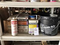 Photo showing various boxes of grout, a grout additive bottle, and large bucket on a shelf