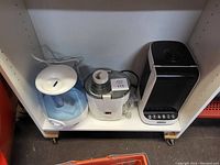 Three small appliances on a shelf: two humidifiers and one Eden Pure heater.