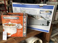 Photo of Proctor Silex slow cooker box and Bella Cucina buffet server box together on a table indoors.