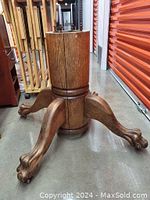 Side view of lion's paw carved wooden table base showing curved legs and octagonal central body with wood grain.