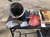 Photo showing white bucket with assorted disposable adhesive applicators and various hand tools on the table, including scrapers and drill bits.