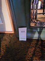 Large rectangular wall mirror with gray frame leaning against a wall, showing part of the room reflected.