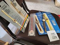 Photo of novelty wristwatches placed on two chairs, showing two slim digital gold-tone watches still sealed in packaging, a santa-themed watch, and three other novelty style watches on blue card backing.