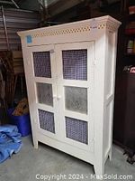 Front view of vintage cream-colored pie safe with closed double doors, featuring blue gingham fabric panels and punched tin pineapple designs.