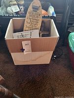 Cardboard box filled with religious decorative items including wooden plaques and crosses. Shows box and contents for reference.