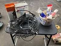 Three roof de-icing cables with two still in boxes, and bucket with assorted ropes and cords on black table.