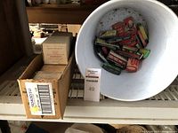 Photo showing 8 boxes of Roberts staples catalog number 10-210 on a shelf next to a white bucket containing multiple smaller boxes of Arrow brand staples.