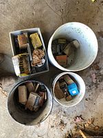 Three buckets filled with assorted staple boxes and a plastic carrier with small boxes and loose nails and screws
