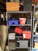 Shelf with multiple toolboxes and tool carriers in plastic, metal, and wood in various sizes and conditions, some rusted.