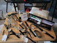 Overview of multiple wristwatches and watch bands on table, including boxed wristwatch with brown leather strap, various watches with leather and metal bands.