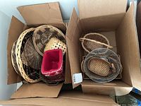 Photo of two cardboard boxes containing a variety of wicker baskets and one visible wire basket, some baskets placed inside others.
