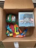 Open cardboard box revealing boxed Deluxe Metal Bingo Cage Set, wooden bingo luck box, and multiple colorful bingo daubers and magnetic wands inside.