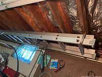Metal extension ladder stored horizontally in basement rafters, showing overall condition and length.