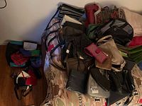 Overview photo showing a variety of handbags and wallets piled on a bed and on the floor.