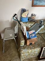 Photo showing shower chair, cane, boxes with blood pressure monitors, aromatherapy packs and slippers on a couch