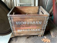 Front view of wooden crate with 'HOFFMAN Beverages' painted text on side, showing metal edge trim and visible wear.