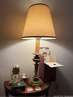 Brass tone metal base lamp with fabric shade illuminated on a wooden table, showing tarnished base.