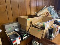 Boxes of assorted office supplies on a wooden surface with key hooks, journals, and other items visible.