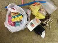 The lot contents showing a sealed package of BIC Sensitive razors, plastic bag with wooden clothes pins, blue and brown hair curlers, black compact binoculars with strap, and tangled brown electrical power cord on carpeted floor.