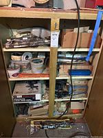 Wooden shelving unit filled with various tools and hardware items including boxed drill, angle grinder, and jigsaws.