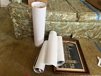 Framed print and five rolled prints arranged on the floor with sofa background. Shows NYC skyline framed art and rolled prints beside it.