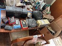 Overview of the lot displayed on a wooden table showing multiple radios, alarm clocks, and a cordless phone with various wires and packaging.