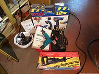 Full view of all items including Ryobi drill set in original packaging, Craftsman tool, Chicago Electric drill, reciprocating saw box, hard hat, ear protection, and battery charger