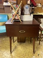 Front view of the closed wooden sewing cabinet with sewing accessories on top and in the box, showing condition and setup.