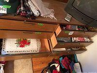 Four open drawers of a wooden dresser showing stacks of cloth and plastic table linens and placemats. A cloth tablecloth with a Christmas floral design is visible in the top drawer.