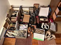 Photo displaying about 18 pairs of women's shoes size 8.5 arranged on floor, including multiple boxes, some shoes wrapped in plastic, variety of styles such as boots, sandals, and dress shoes.