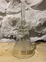 Full view of the tall clear glass bell with etched sailing ship and detailed glass handle on a stone background.