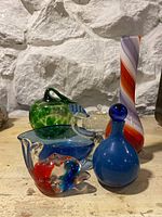 Photo showing the green apple glass piece, blue bowl, clear dolphin figurine with blue accents, blue decanter with stopper, and tall striped vase.