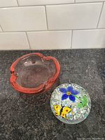 Photo showing red-toned art glass bowl and clear glass paperweight with blue flower and yellow butterfly embedded inside.
