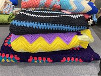 Three folded crochet blankets stacked, showing colorful zigzag and stripe patterns