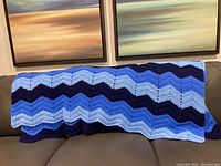 Entire blue crochet blanket throw draped over couch, showing repeating zigzag pattern in various blues.